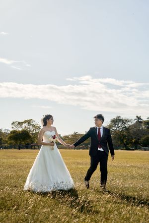 Bride and groom holding hands in sunlit meadow during golden hour.