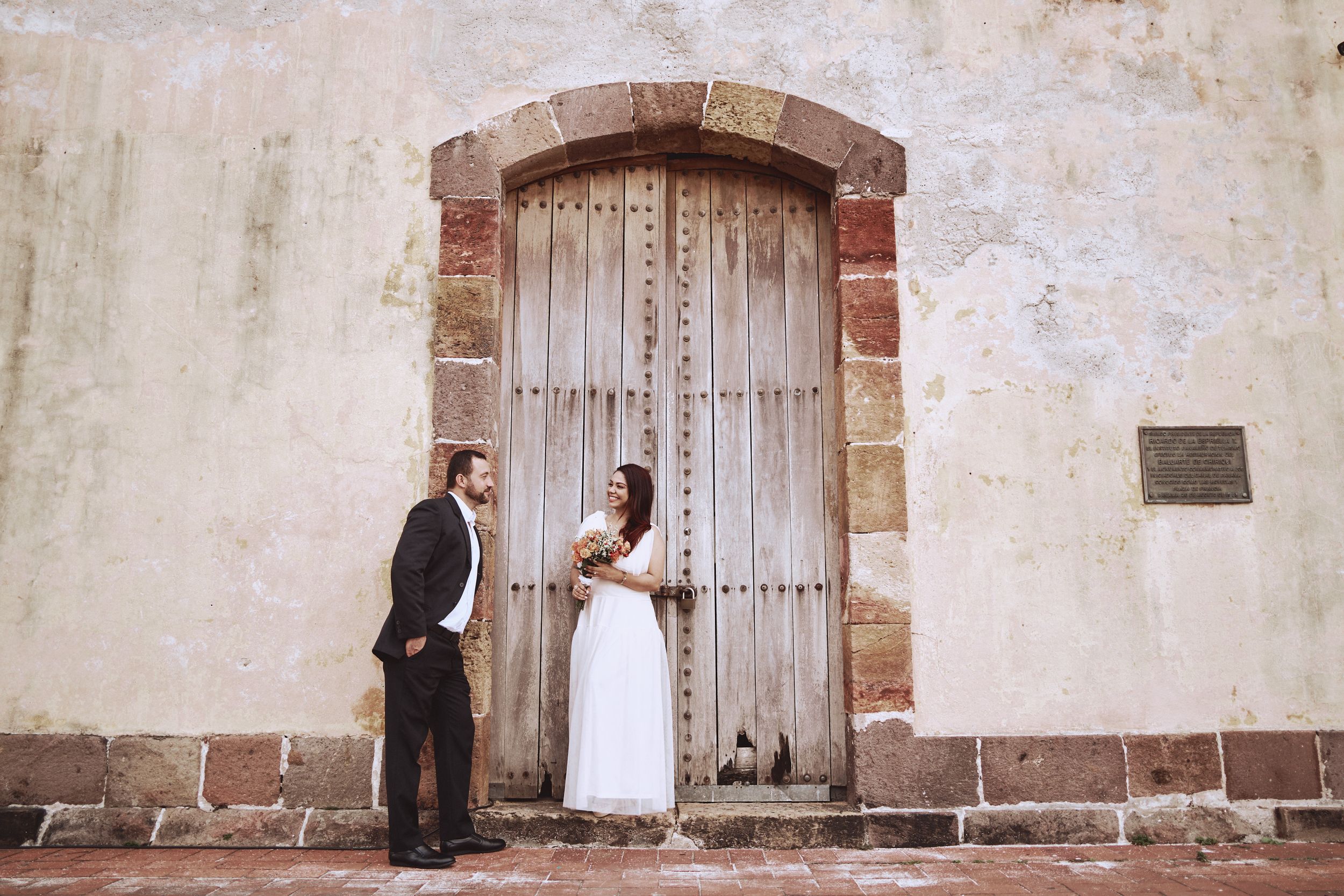 Wedding couple poses against rustic wooden colonial door and stone archway.