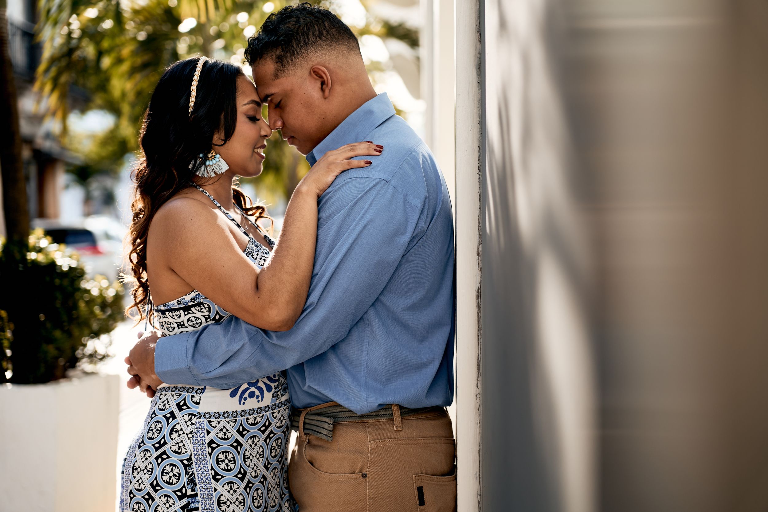 An intimate engagement photo against a white wall with natural lighting.