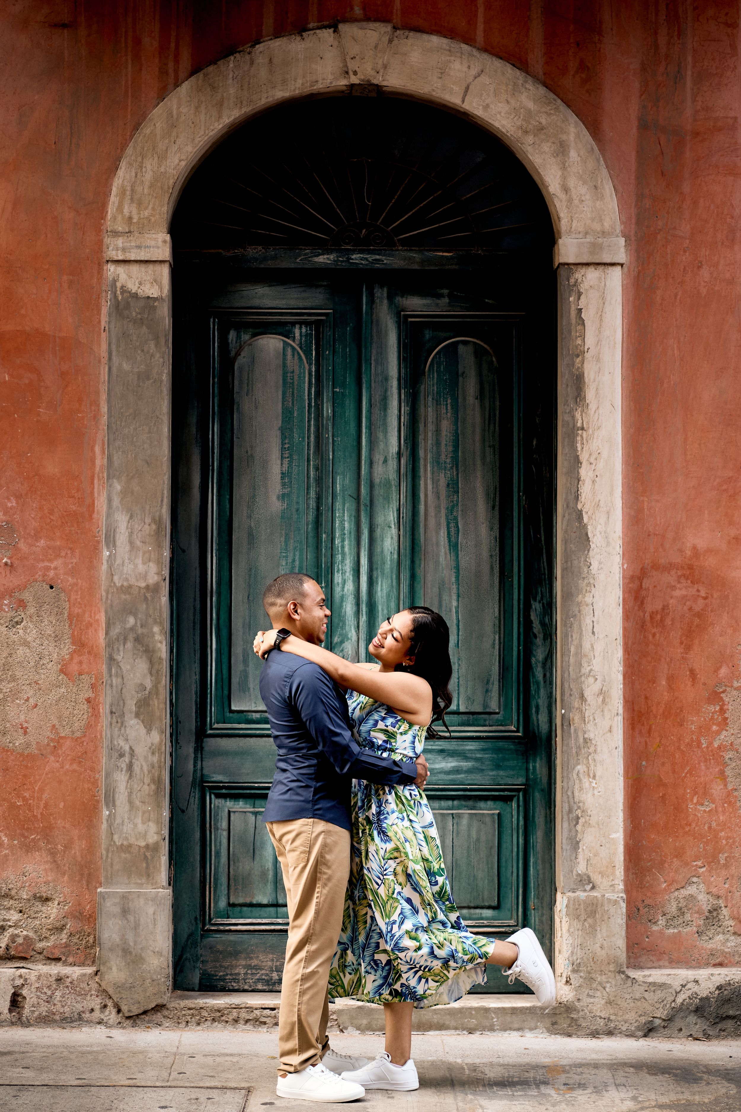 A couple sharing a romantic moment in front of a vintage green door with terracotta walls.