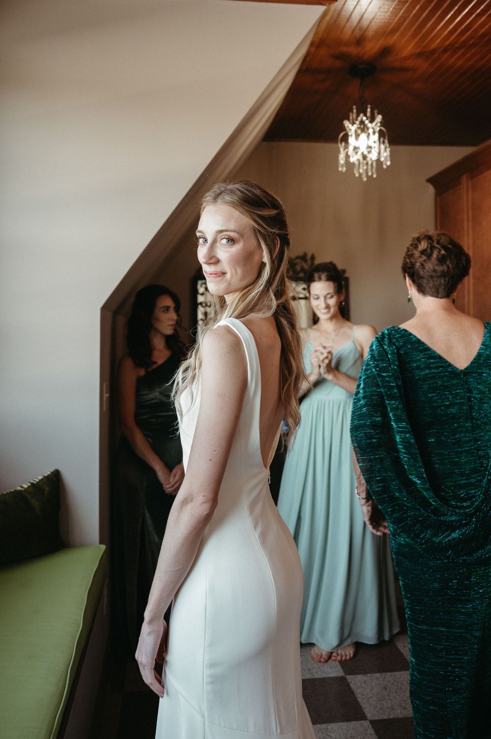 An elegant bride in a fitted white dress poses with others in an interior setting with a chandelier.