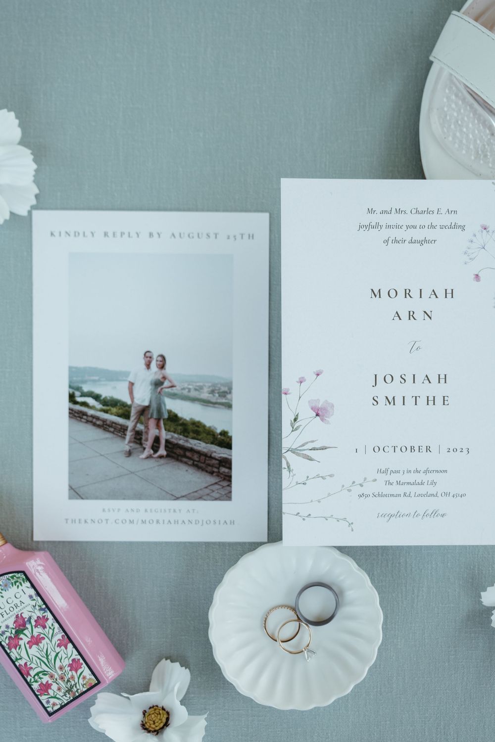 Wedding invitation suite with rings on white shell dish and floral accents.