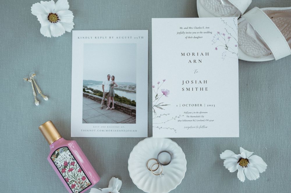 Minimalist wedding stationery layout with rings and white flowers on grey background.