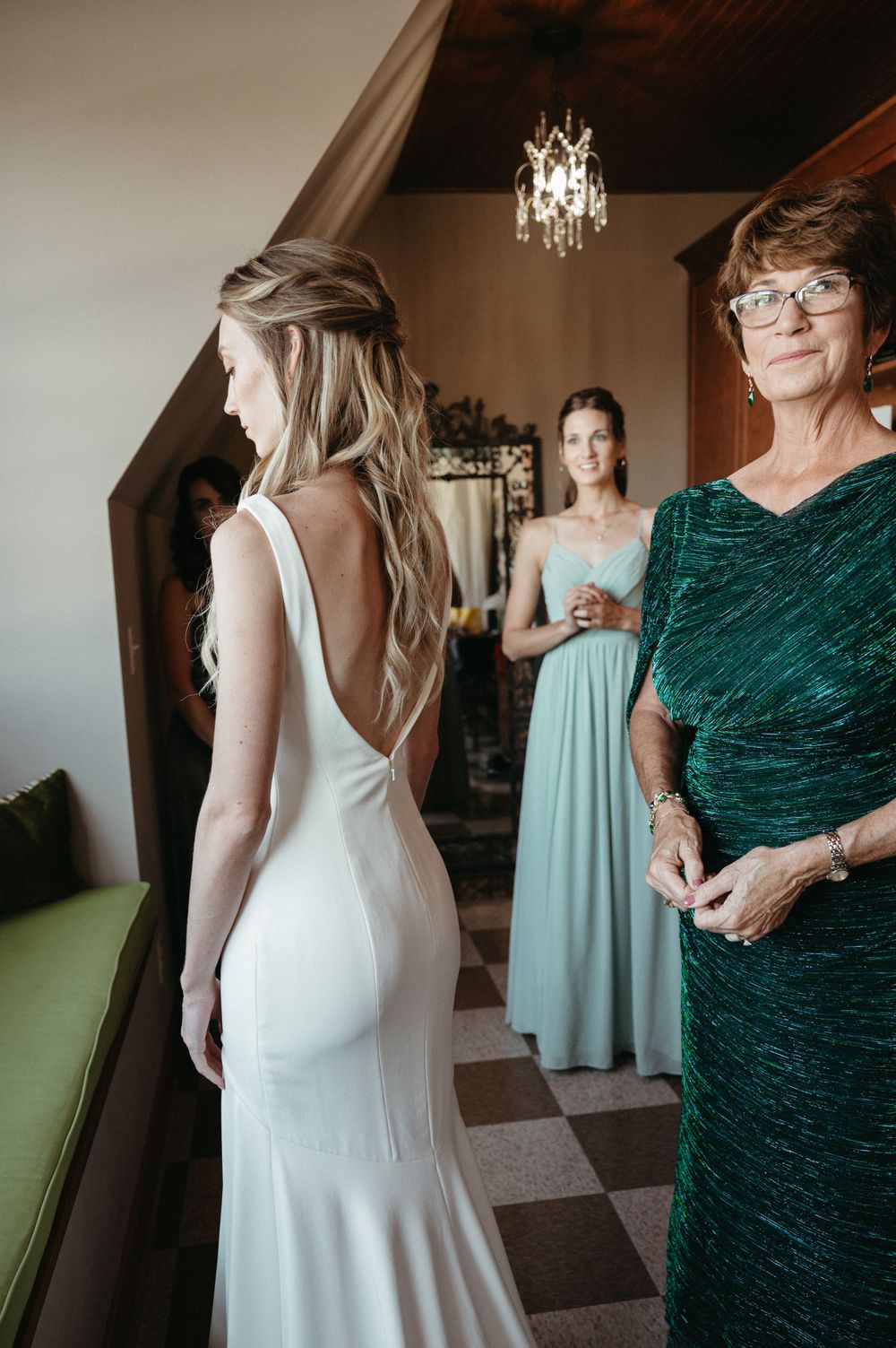 A wedding dress fitting scene showing the backless design with attendants in green dresses nearby.