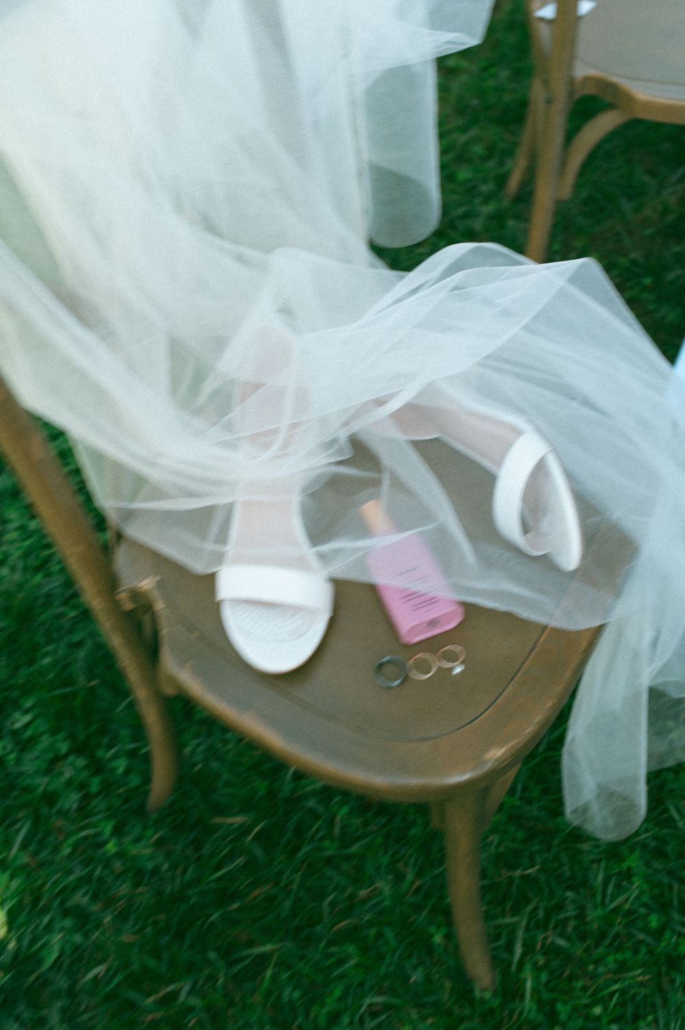 Wedding details with white bridal shoes and veil draped over a vintage chair.