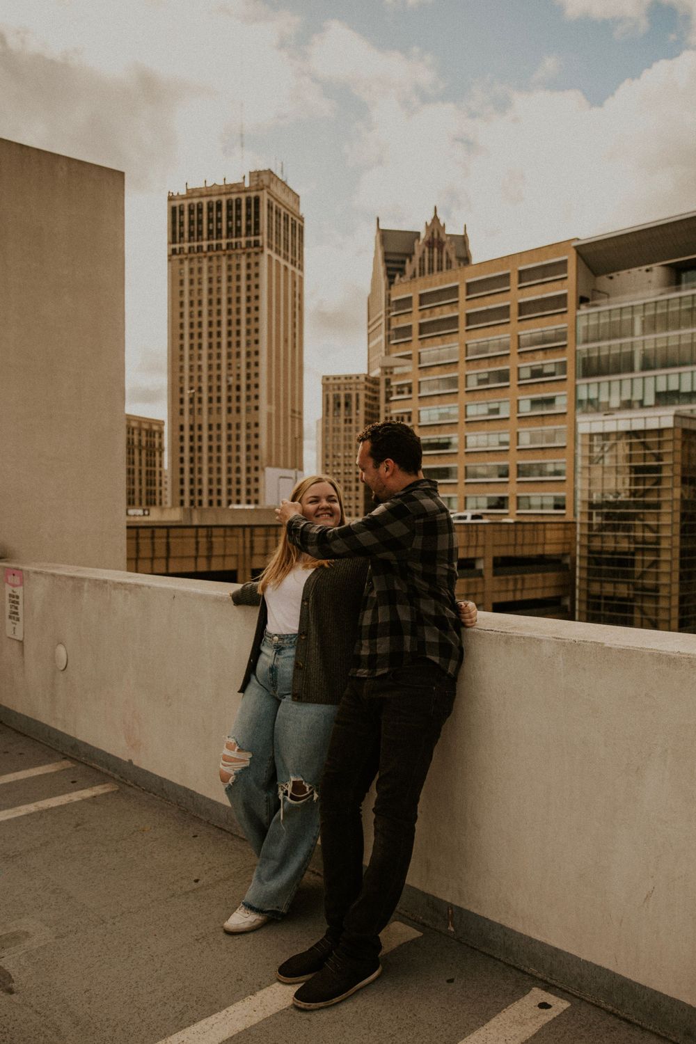 Inner-city engagement session. Couple looks at each other in front of Detroit skyline.