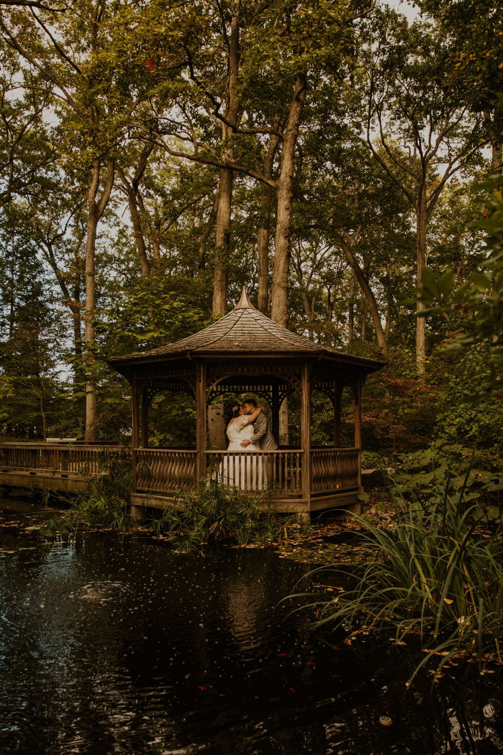Botanical garden intimate wedding in Toledo. Couple in wedding attire kisses in gazebo across pond.