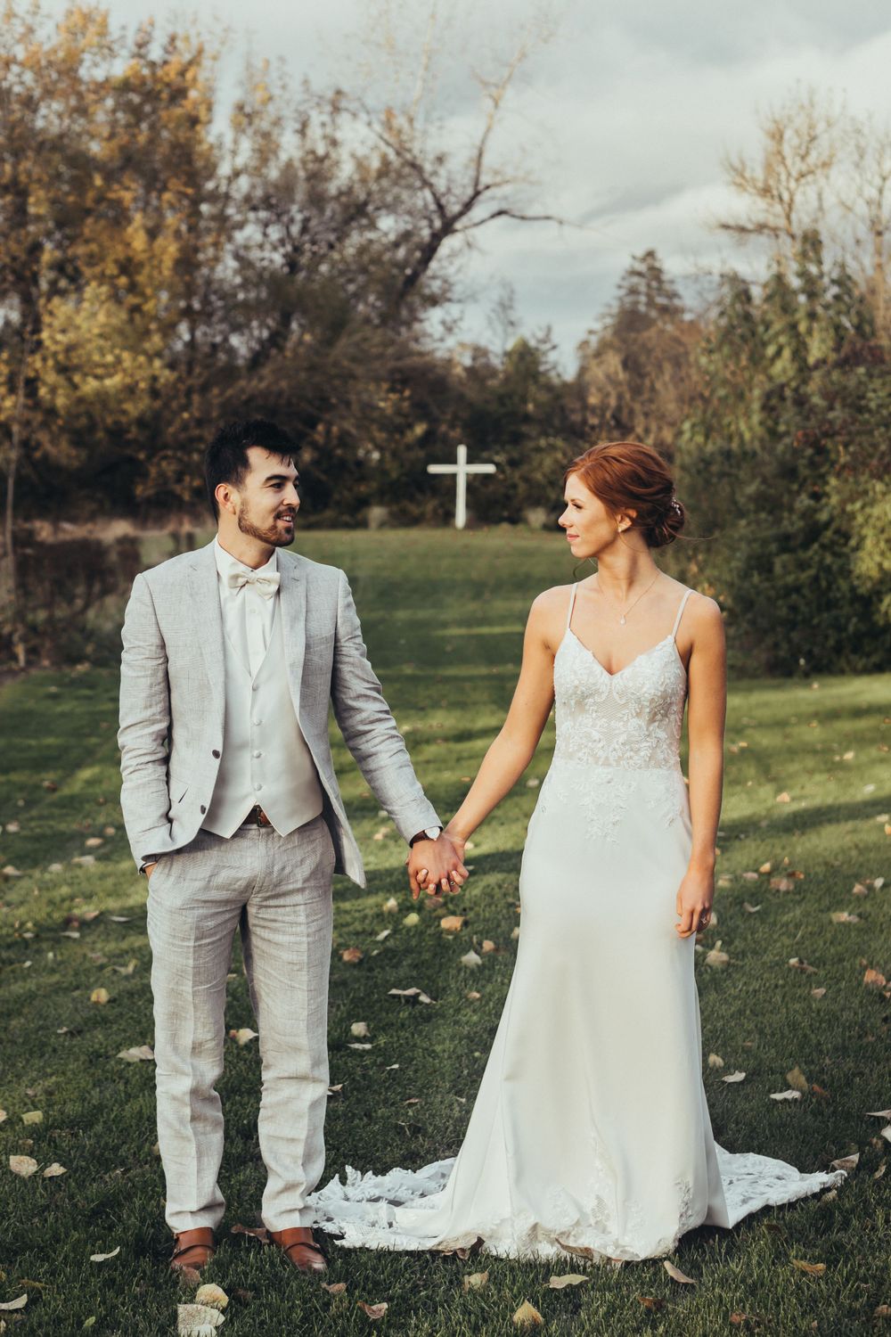 bride and groom stand hand in hand with a cross on the background