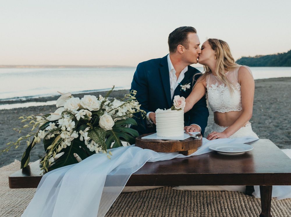bride and groom kiss and cut wedding cake wedding florals and wedding cake with ocean backdrop wedding photos elopement