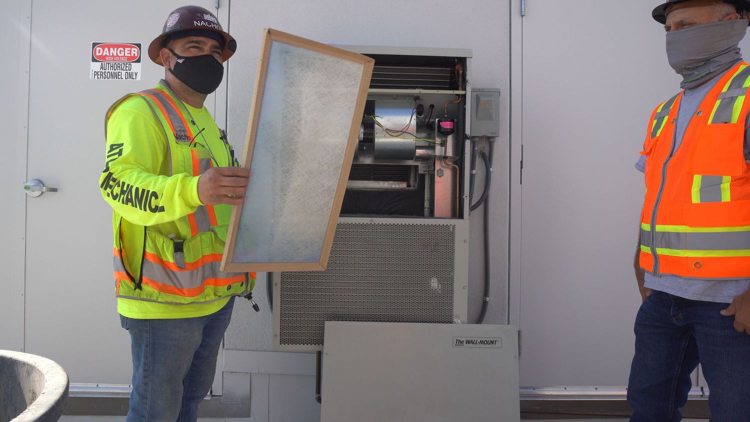 Professional HVAC technician in high-visibility gear demonstrating an air filter replacement for an open industrial air conditioning unit.
