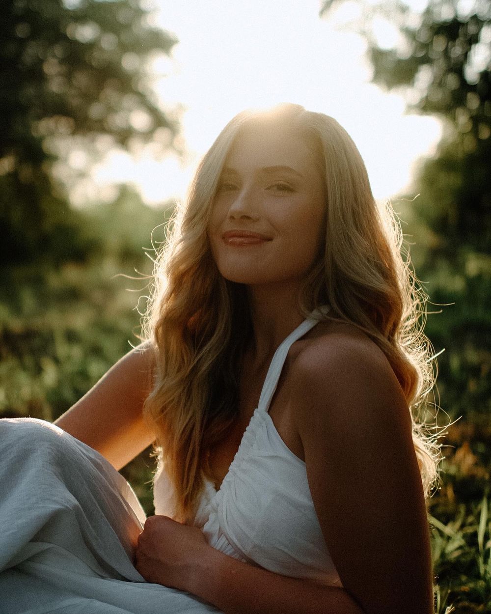A dreamy backlit portrait of a woman in white clothing at sunset with glowing golden light through trees.