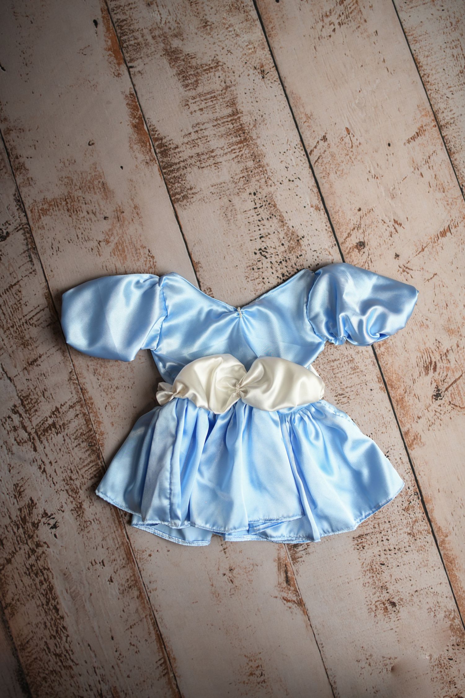 Light blue satin dress with ruffled details on distressed wooden background.