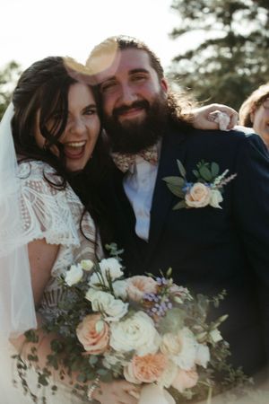 Joyful wedding moment captured in natural light with peach and white floral bouquet.