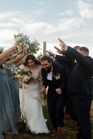 Wedding party forms a tunnel with raised arms for newlyweds to walk through.