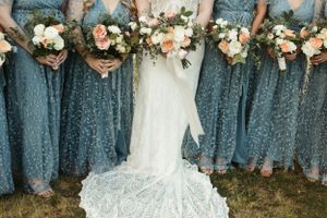 Bridesmaids in blue sequin dresses hold peach and white floral bouquets.