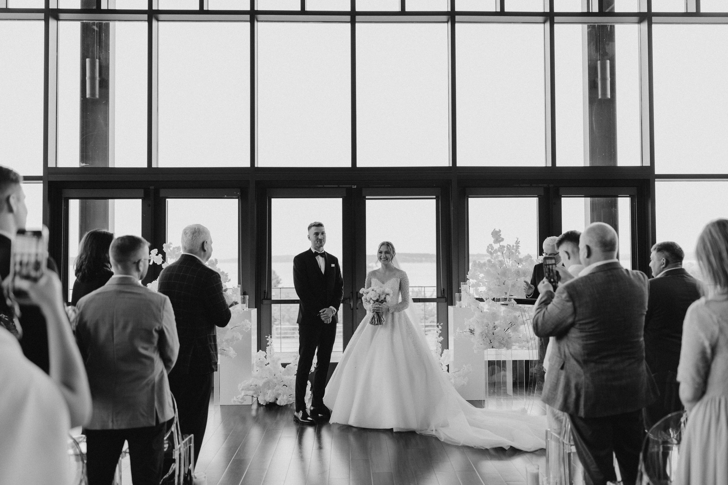 Wedding ceremony taking place in a modern venue with large windows and elegant decor.