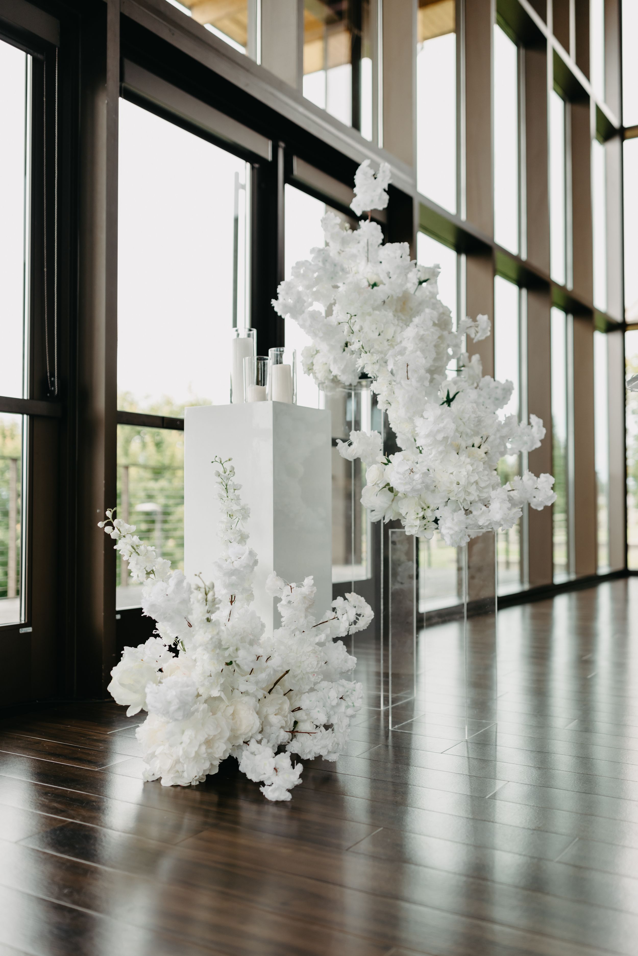 White floral decorations hang elegantly against floor-to-ceiling windows in a modern event space.