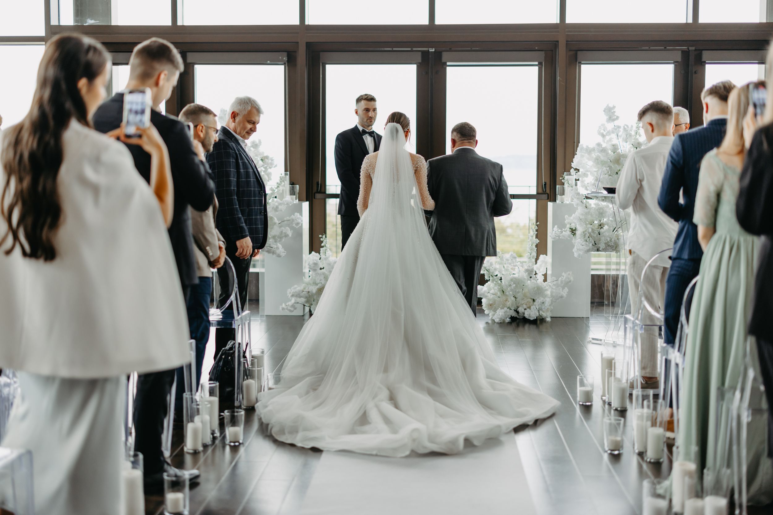 Wedding ceremony in progress with elegant white floral decorations and gathered guests.