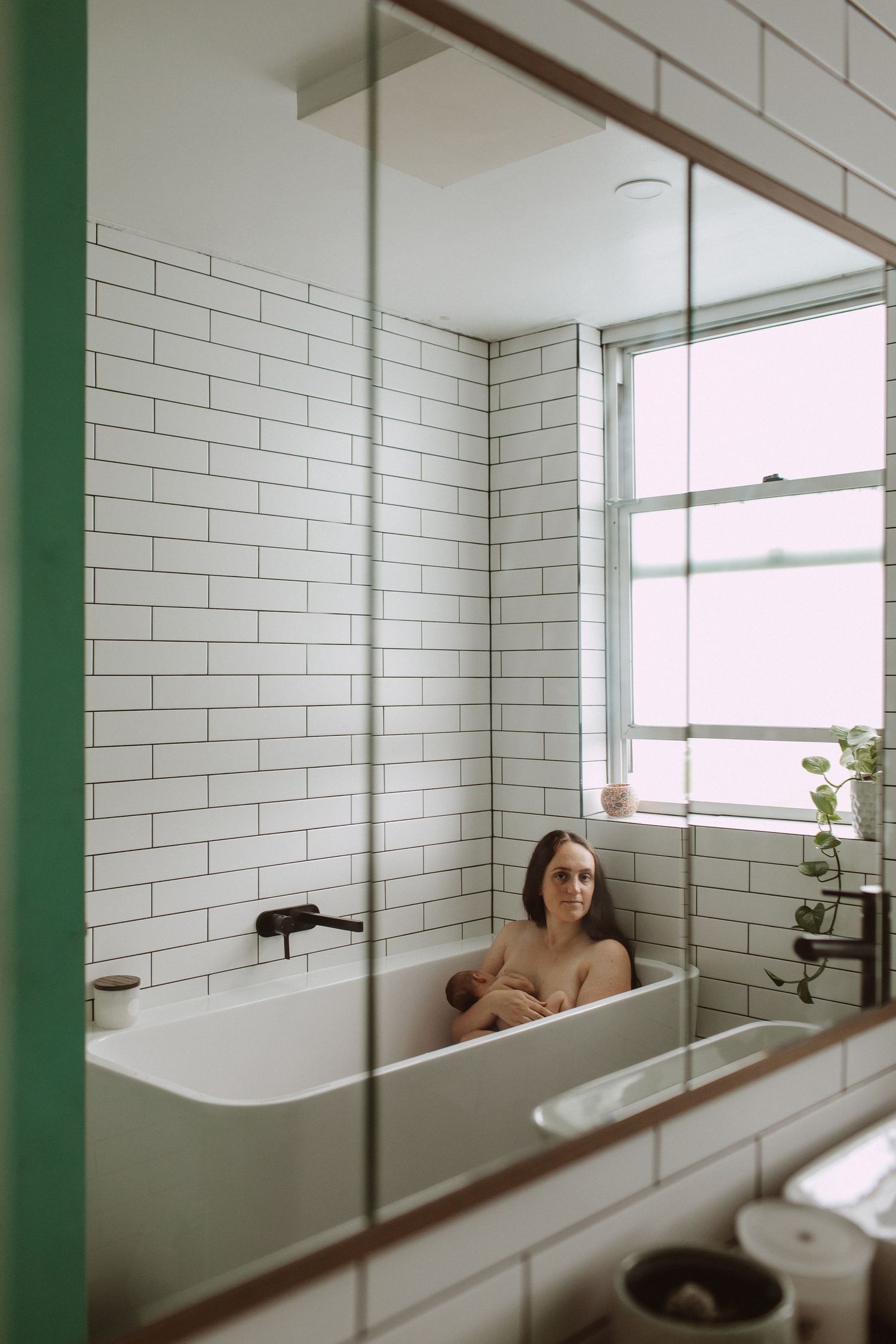 Woman relaxing in a modern white subway tile bathtub photographed through a large mirror reflection.