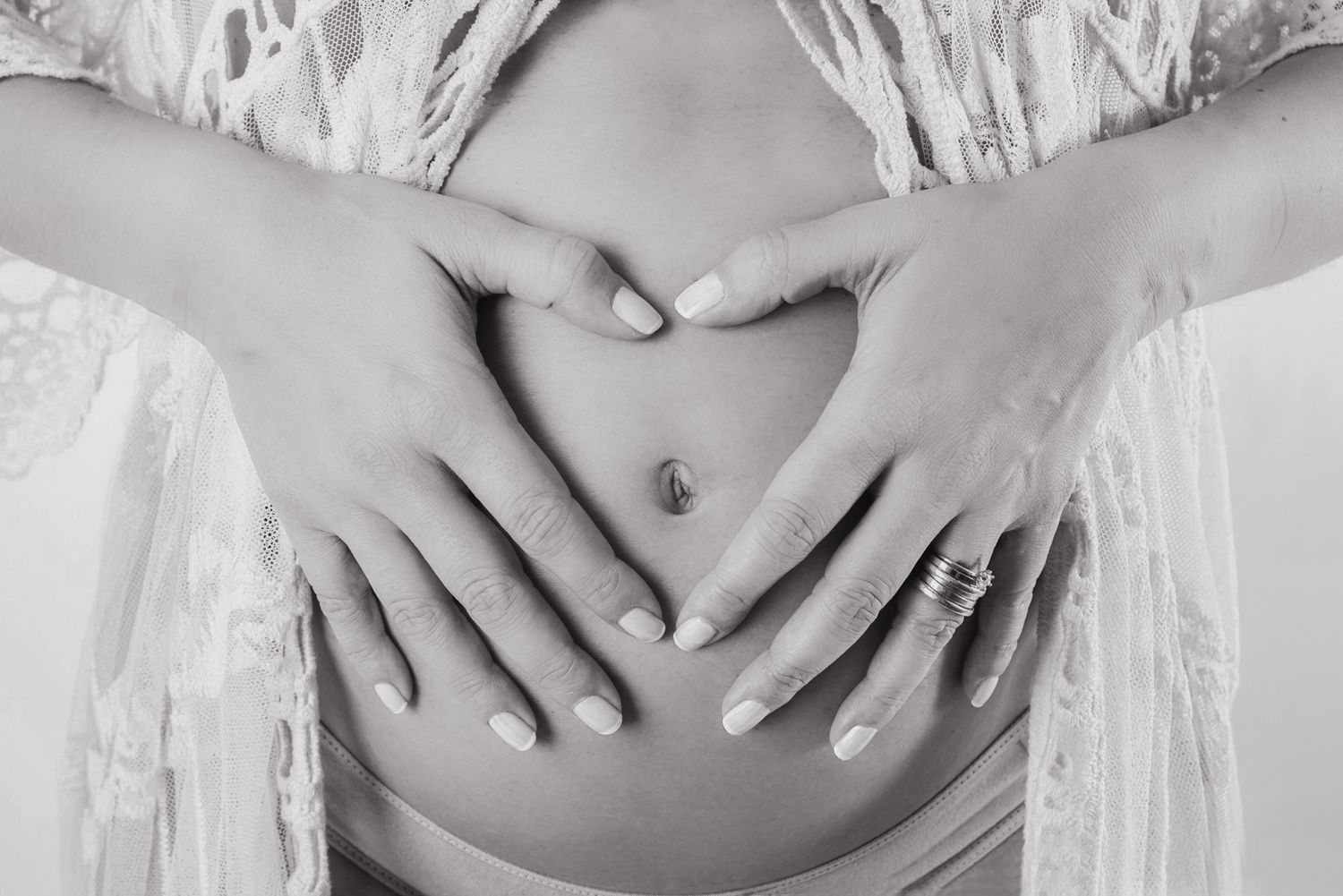 Black and white photo of pregnant woman forming heart shape with hands on baby bump.