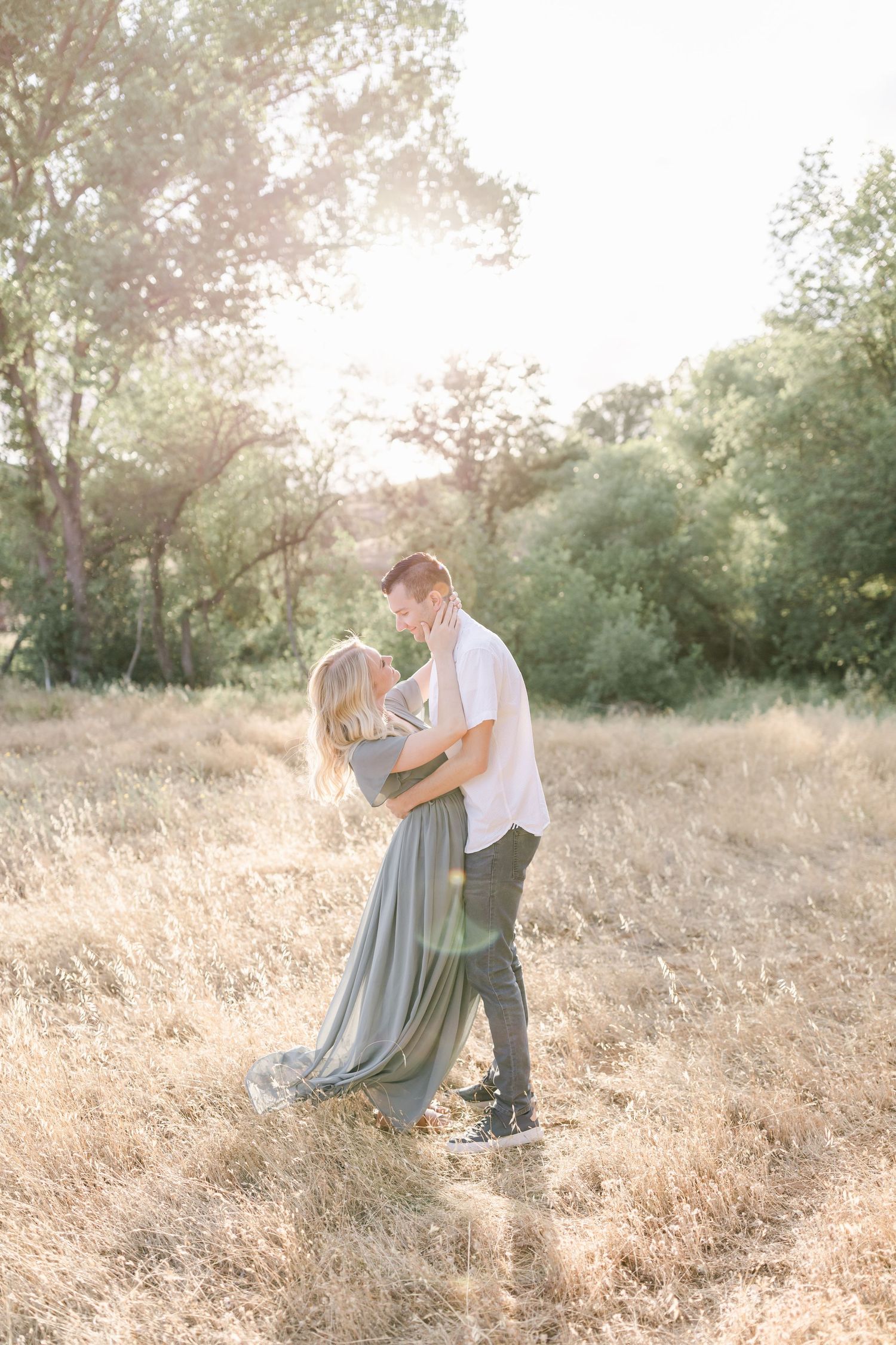 Couple embracing in golden sunlit field during sunset photoshoot.