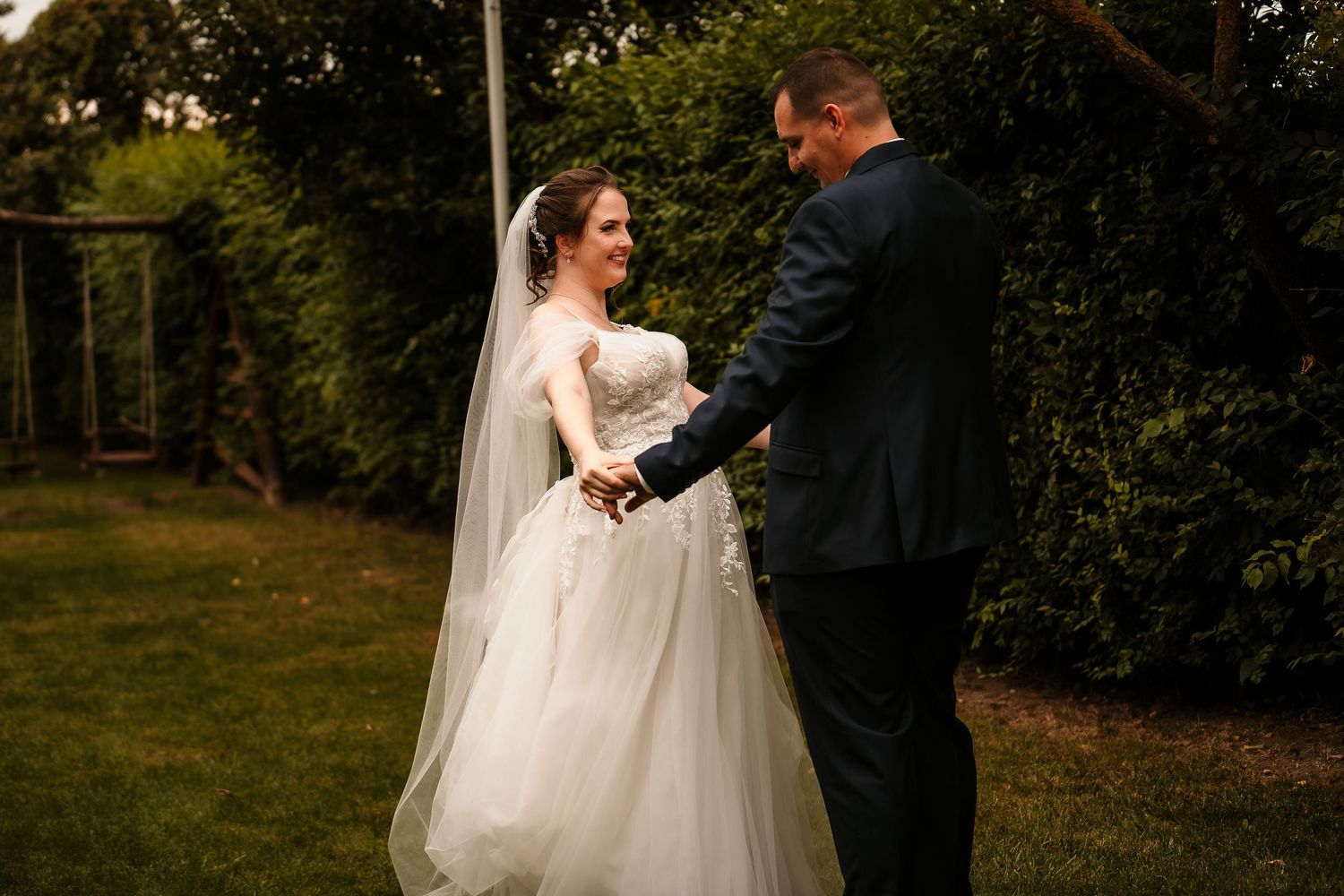 A wedding couple shares a joyful moment together in a garden setting during golden hour.
