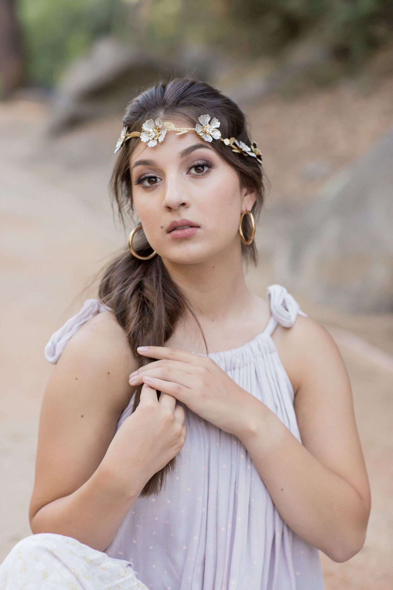 Young woman wearing a gold floral crown headpiece and lavender top posing outdoors near rocks.
