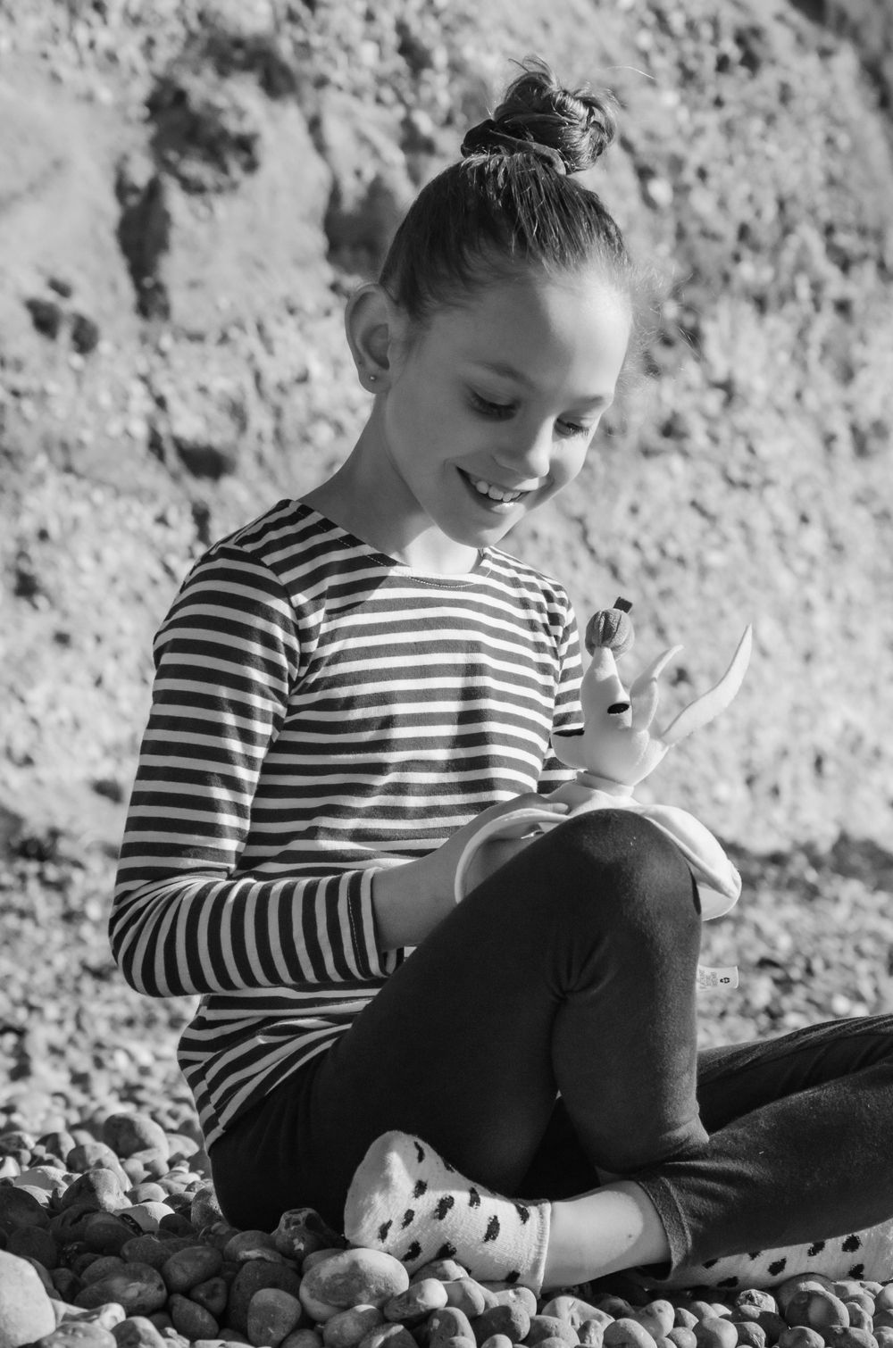 young girl sat crossed legged on pebble beach playing with her cuddly toy