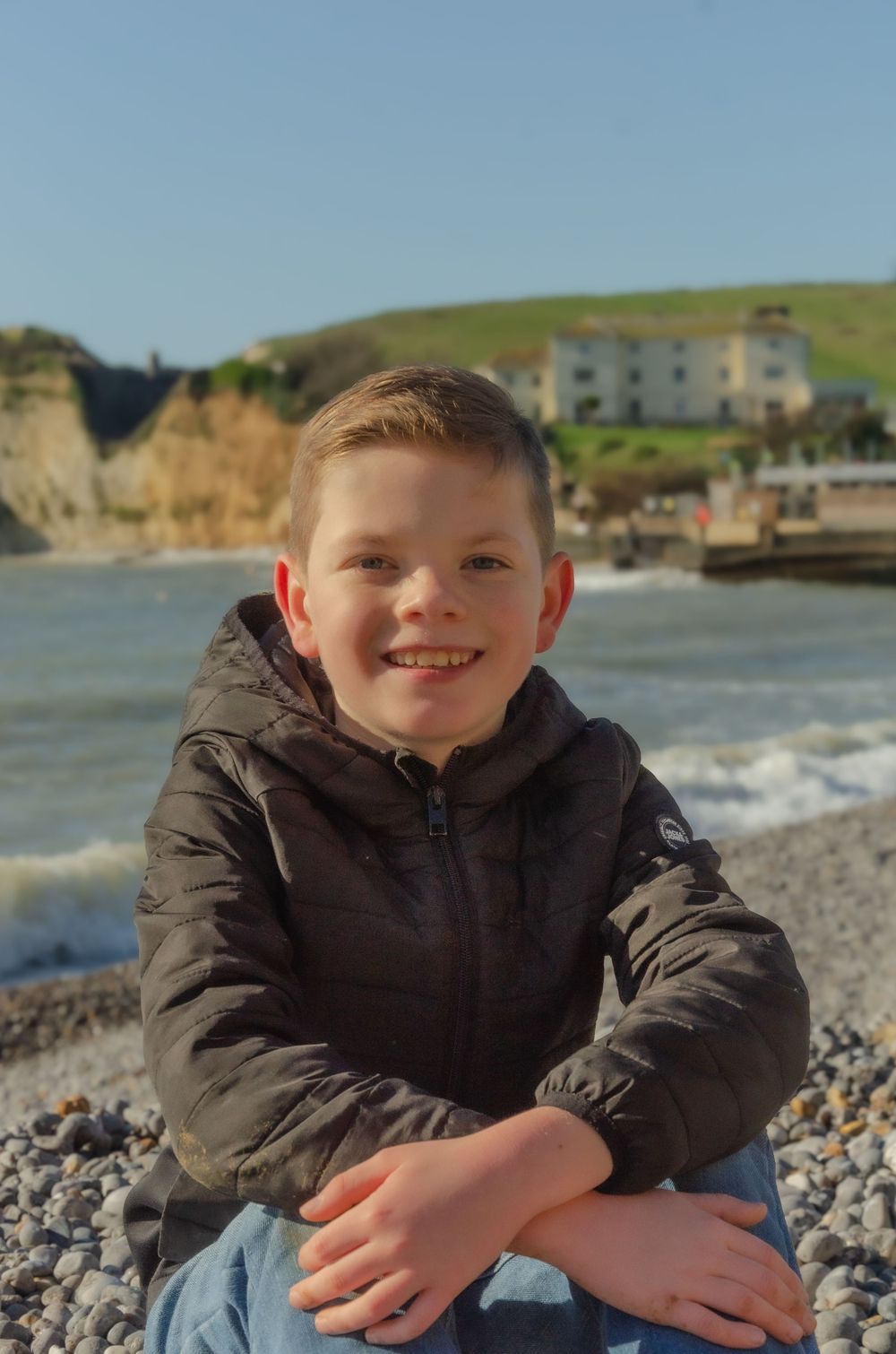 young boy sat on pebble beach smiling