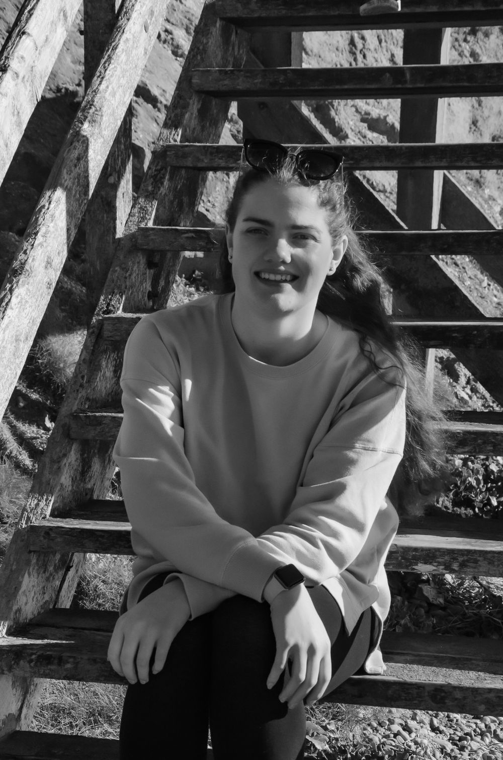black and white portrait of young woman smiling, sat on beach steps