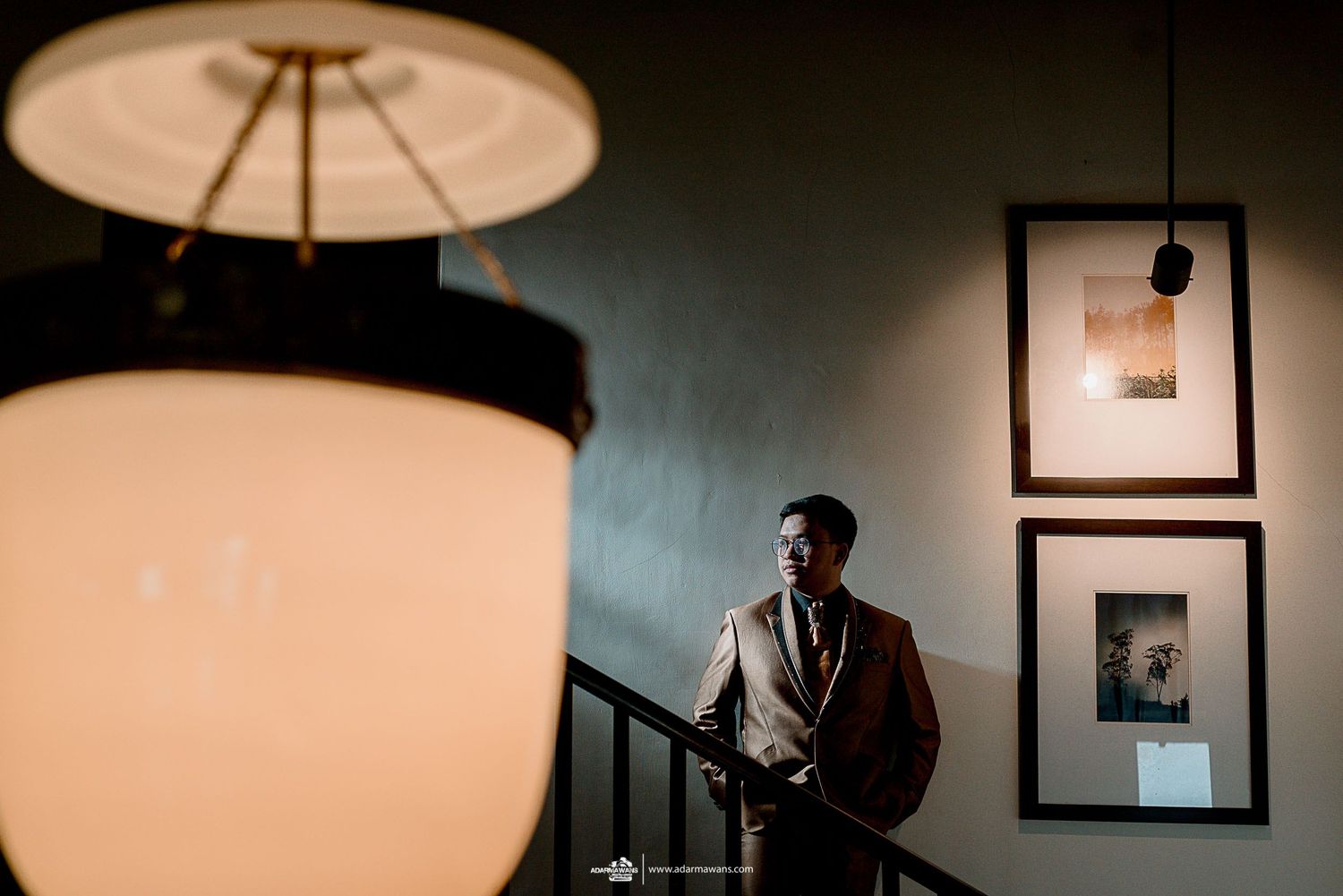 Silhouette by large lamp with framed artwork on wall in moody lighting.