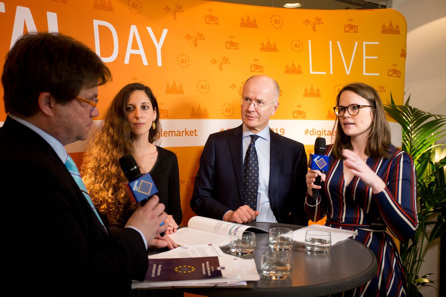 Business professionals participate in a panel discussion against an orange backdrop with text reading 'DAY LIVE'.