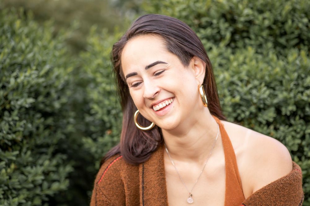 Portrait in natural setting with brown cardigan and gold hoop earrings.