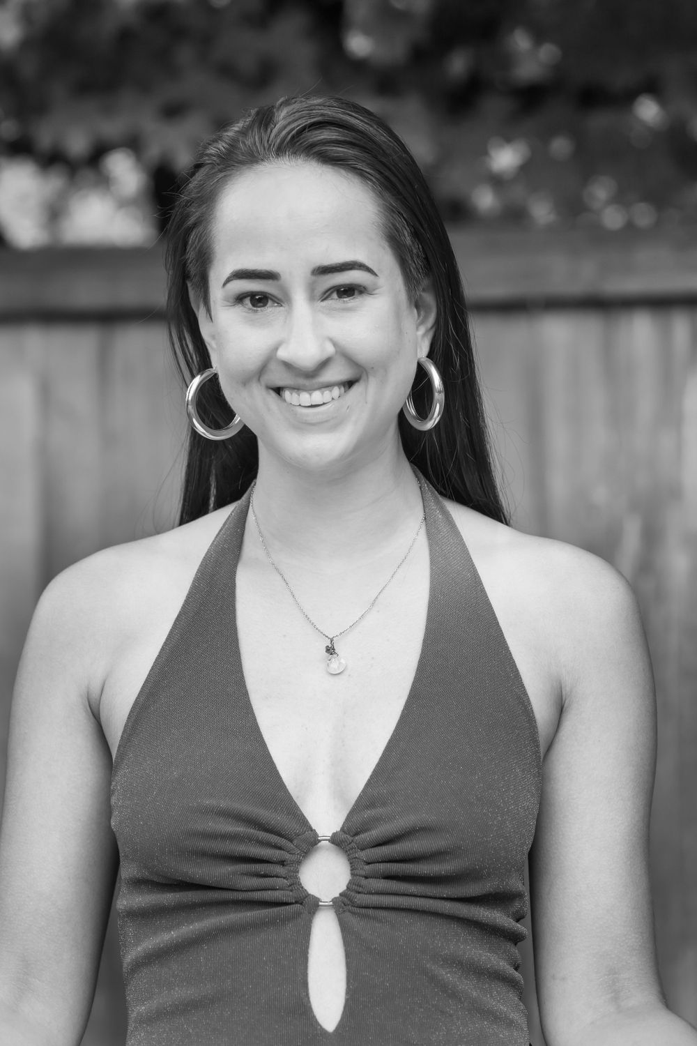 Black and white portrait shot of model in dark halter top with statement earrings against wooden fence.
