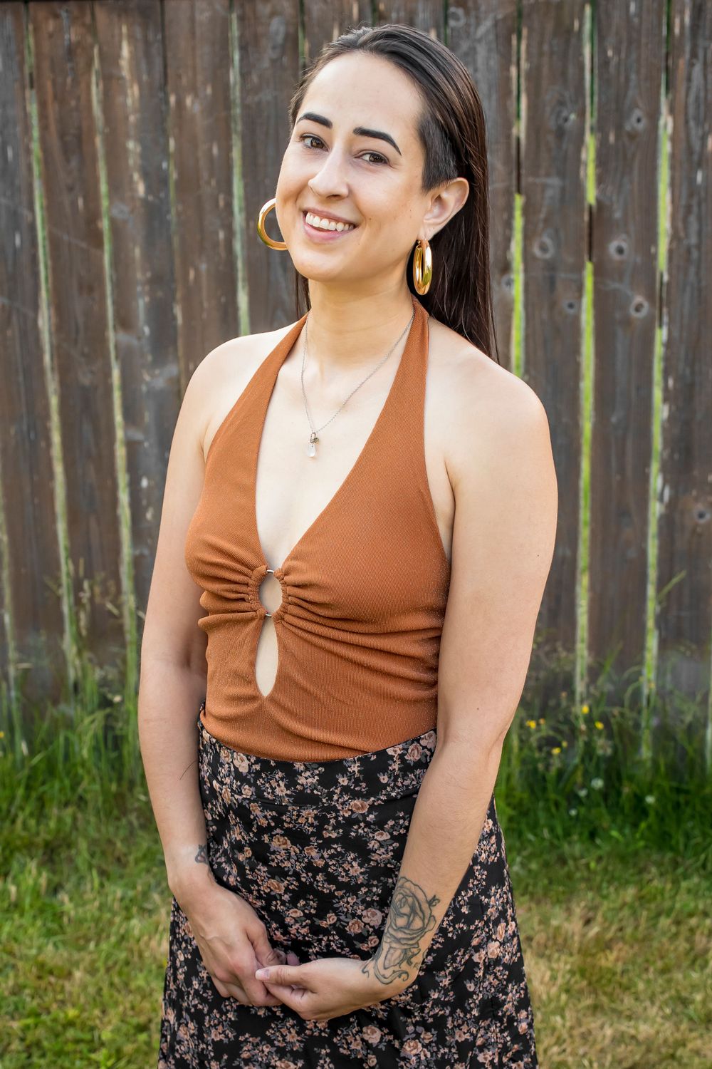 Model wearing brown halter top and floral skirt poses in front of rustic fence.