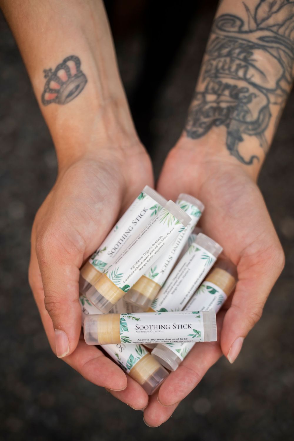 Tattooed hands holding multiple soothing stick balms with natural ingredients.