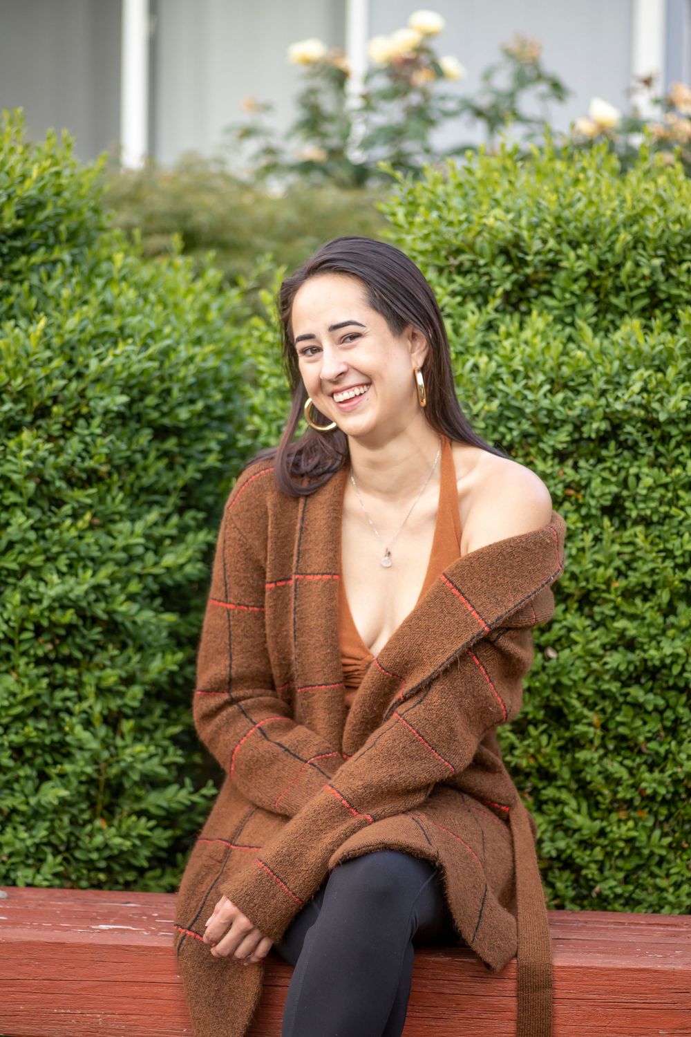 Casual outdoor portrait with cozy brown cardigan against green garden background.
