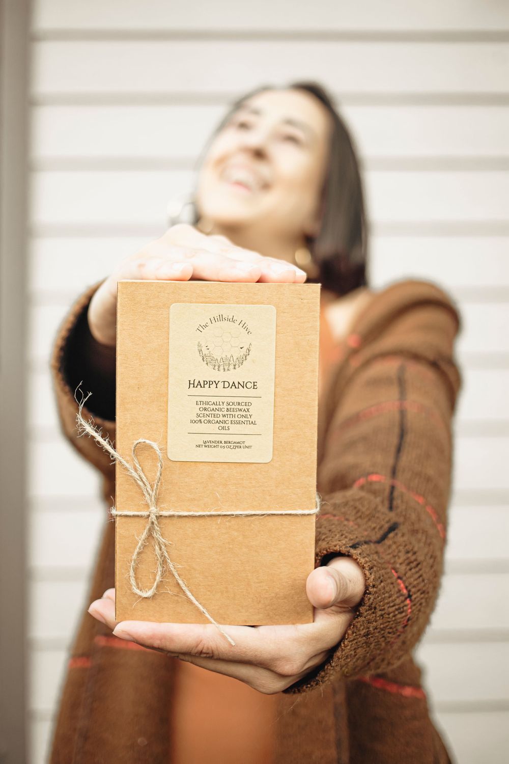 Natural beauty product in kraft paper packaging held up against white wall.