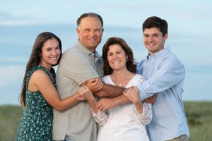 Family of four poses together against blue sky background at sunset.