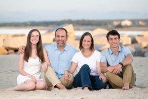 A family sits together on rocks by the beach at sunset.