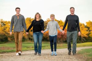 Family of four walking together holding hands on a dirt path during autumn.