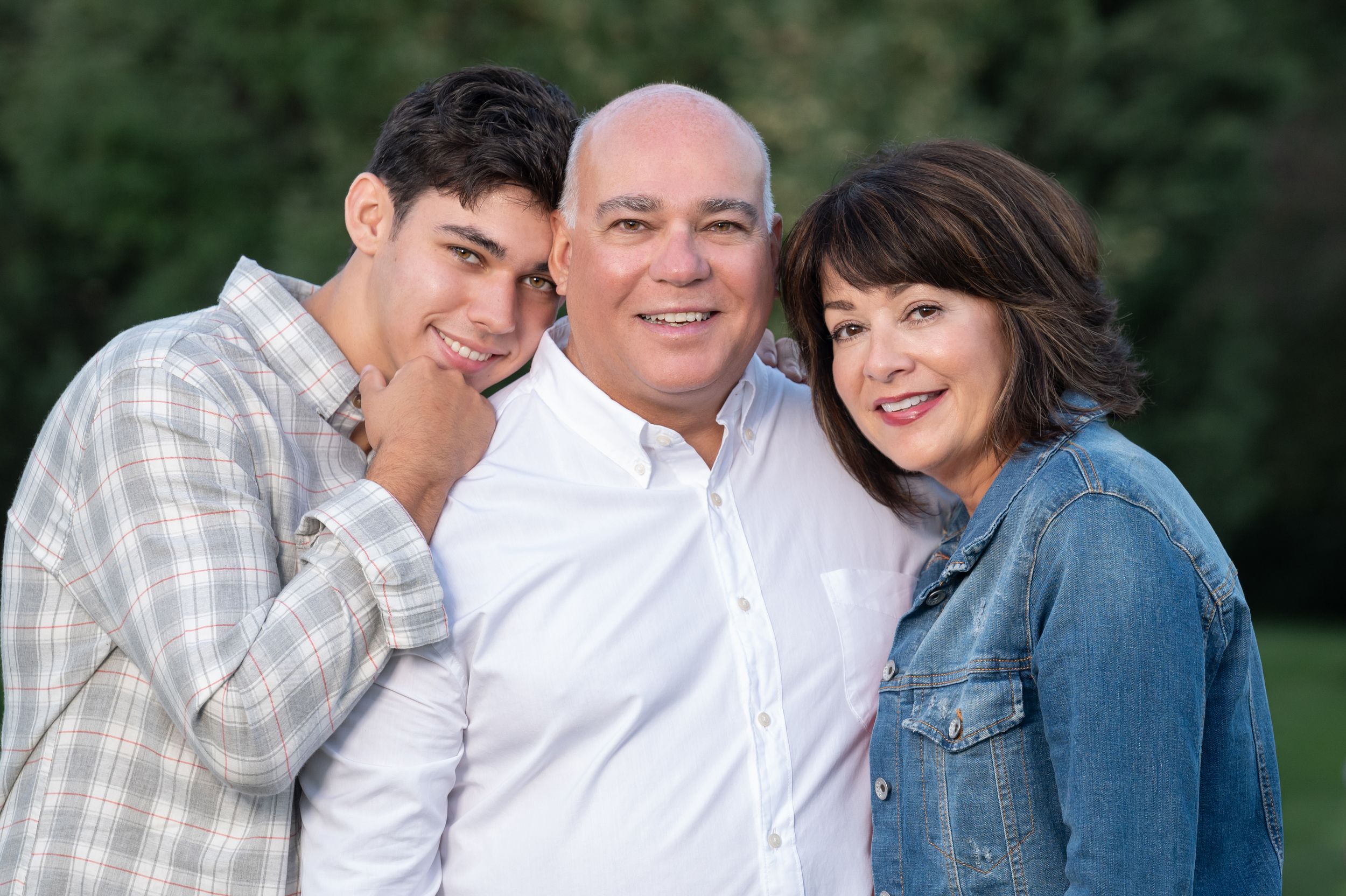 A family of three poses together outdoors in casual attire.