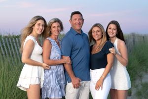 Group portrait of five people in coordinated white and blue outfits against a coastal backdrop at dusk.