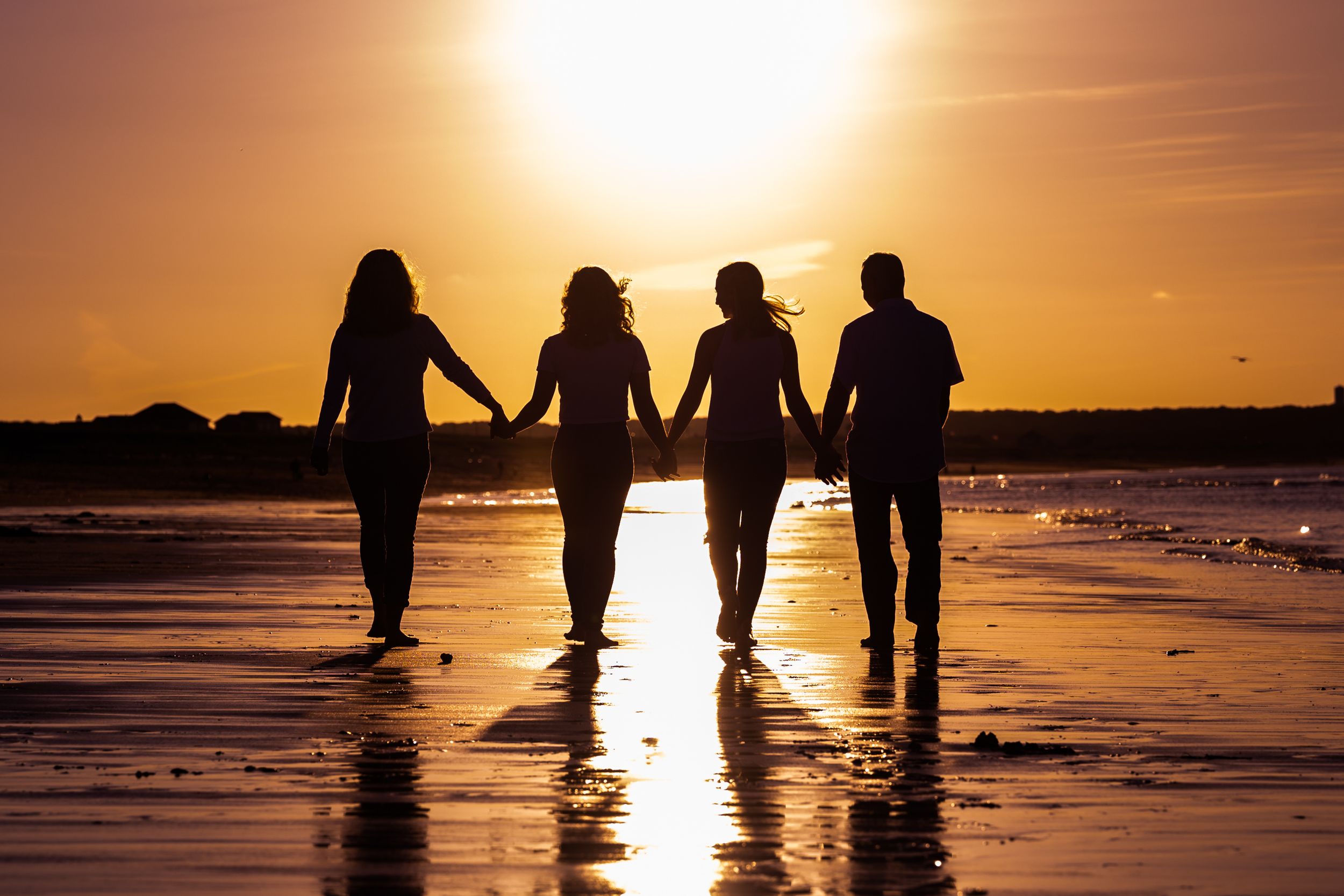 A group of silhouetted figures holding hands while walking on a beach during a golden sunset.