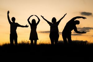 Four silhouettes strike playful poses against a golden sunset sky on a hilltop.