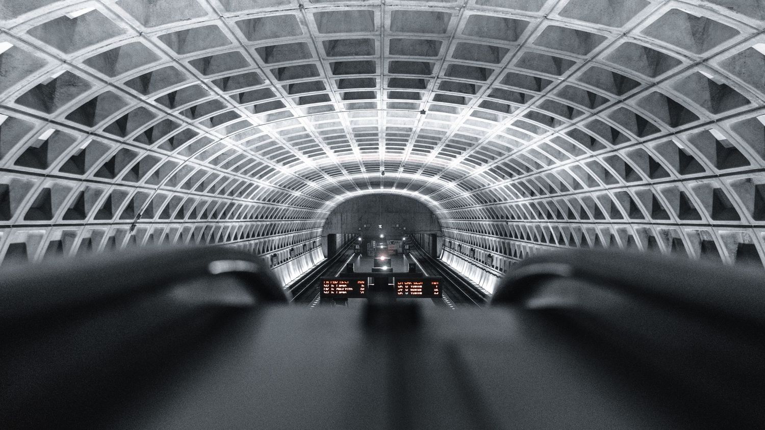 Symmetrical view of a Washington DC Metro station tunnel with vaulted concrete ceiling and escalators.
