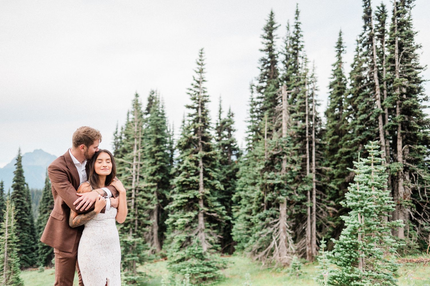 bride and groom snuggling near evergreen trees. Photo by Bremerton wedding photographer.