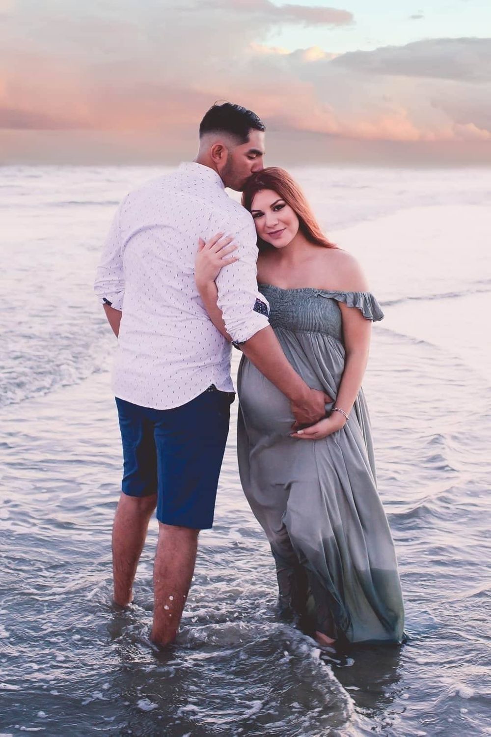 Pregnant wife leaning on husbands shoulder and husband kissing her head while hold pregnant belly in Galveston Tx