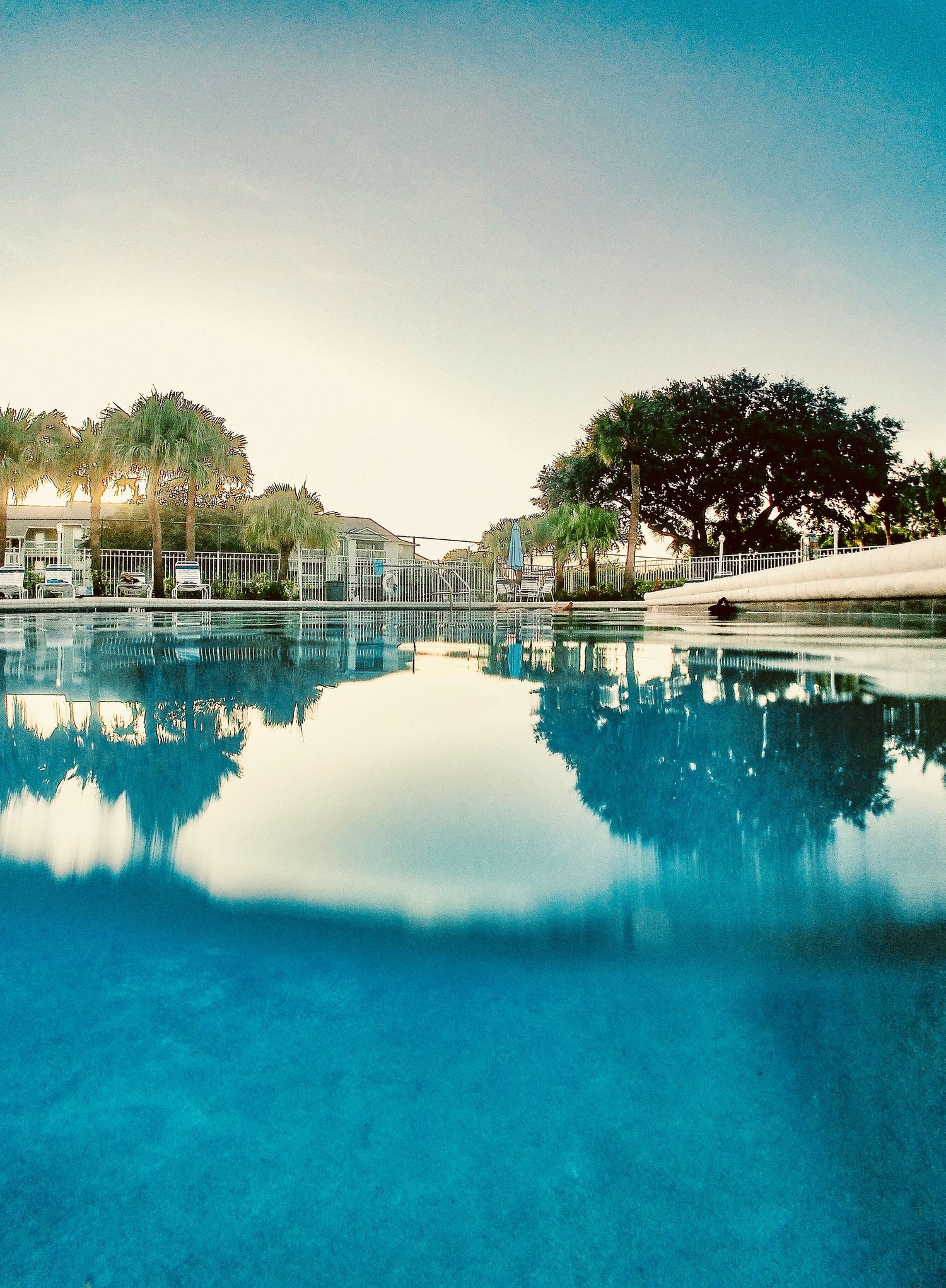 Panoramic view of a pristine blue swimming pool with resort buildings in the background.