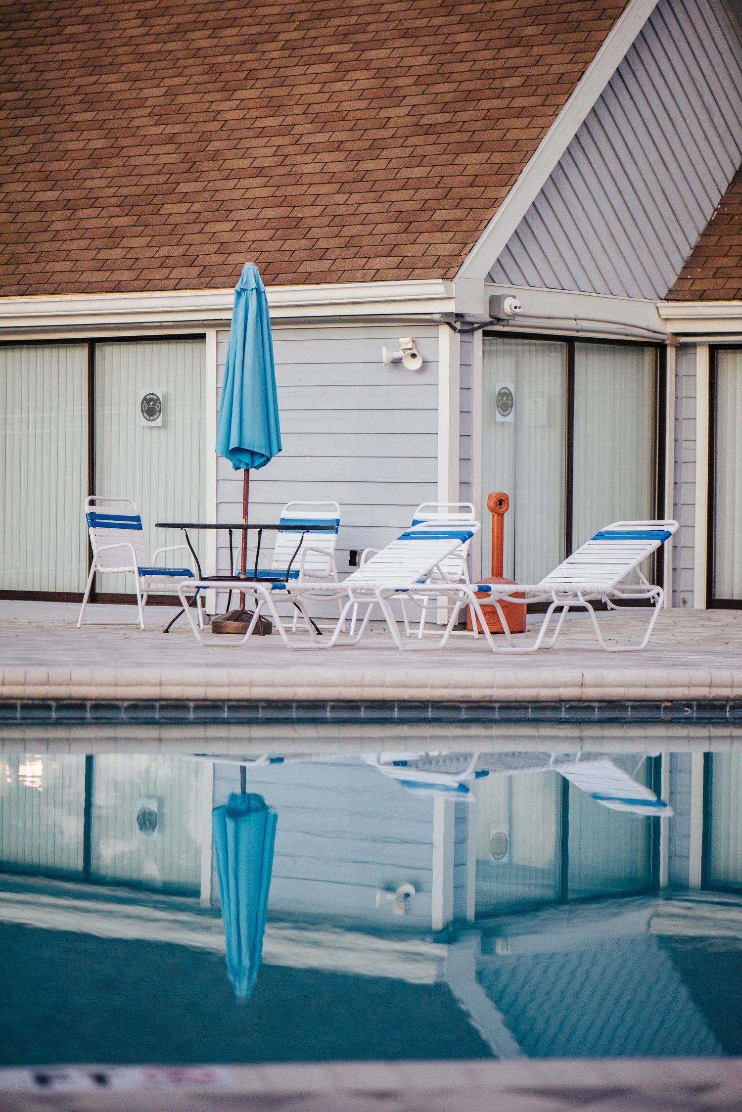 Empty poolside lounge chairs and umbrellas line a swimming pool at a hotel or resort.